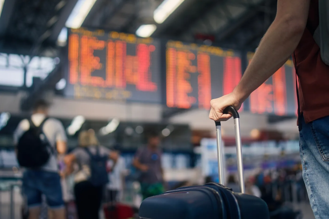 A traveler pulling a suitcase past an arrivals board